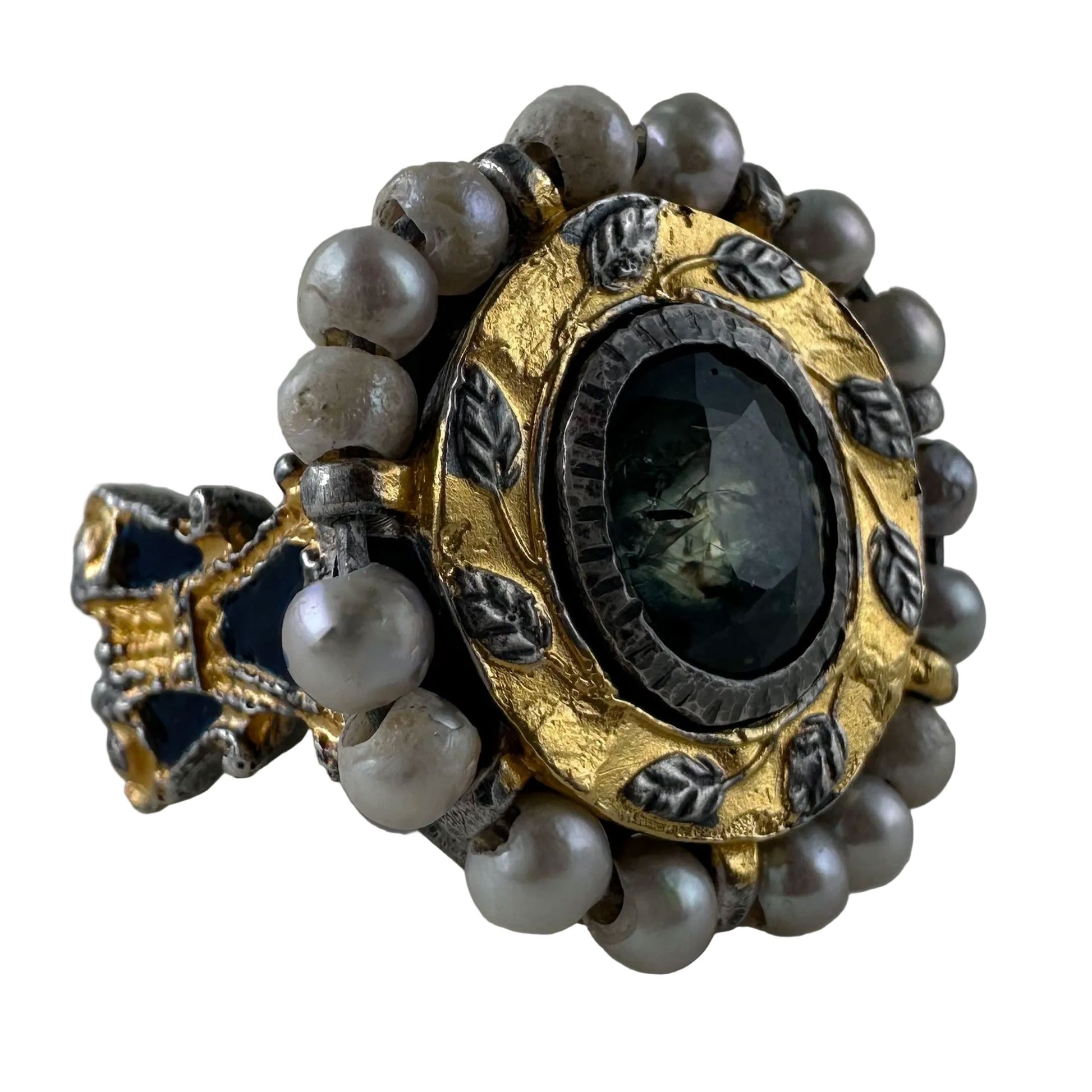 An antique-style ring featuring a round dark green faceted gemstone in a gold and silver-toned setting, surrounded by a border of gray pearls.